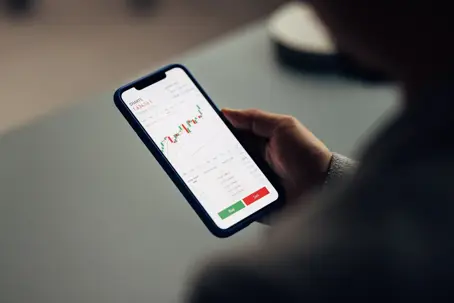 Over-the-shoulder view of a person analyzing stock market charts on a smartphone,